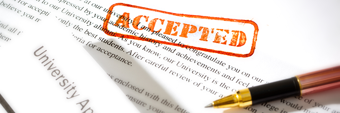An acceptance letter from a university application. An university application form together with the letter of acceptance with a red rubber stamp of "Accepted" on a table top still life. Photographed close-up in horizontal format with selected focus on the rubber stamp impression.