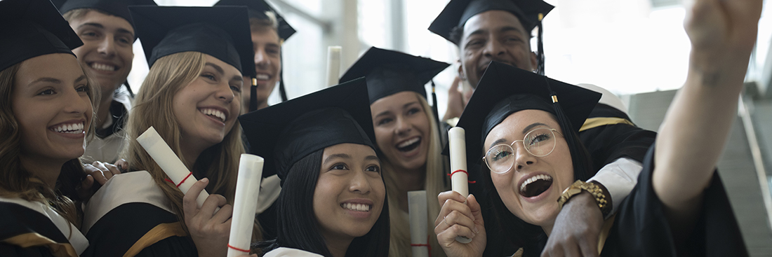 College student graduate friends in caps and gowns taking selfie with camera phone